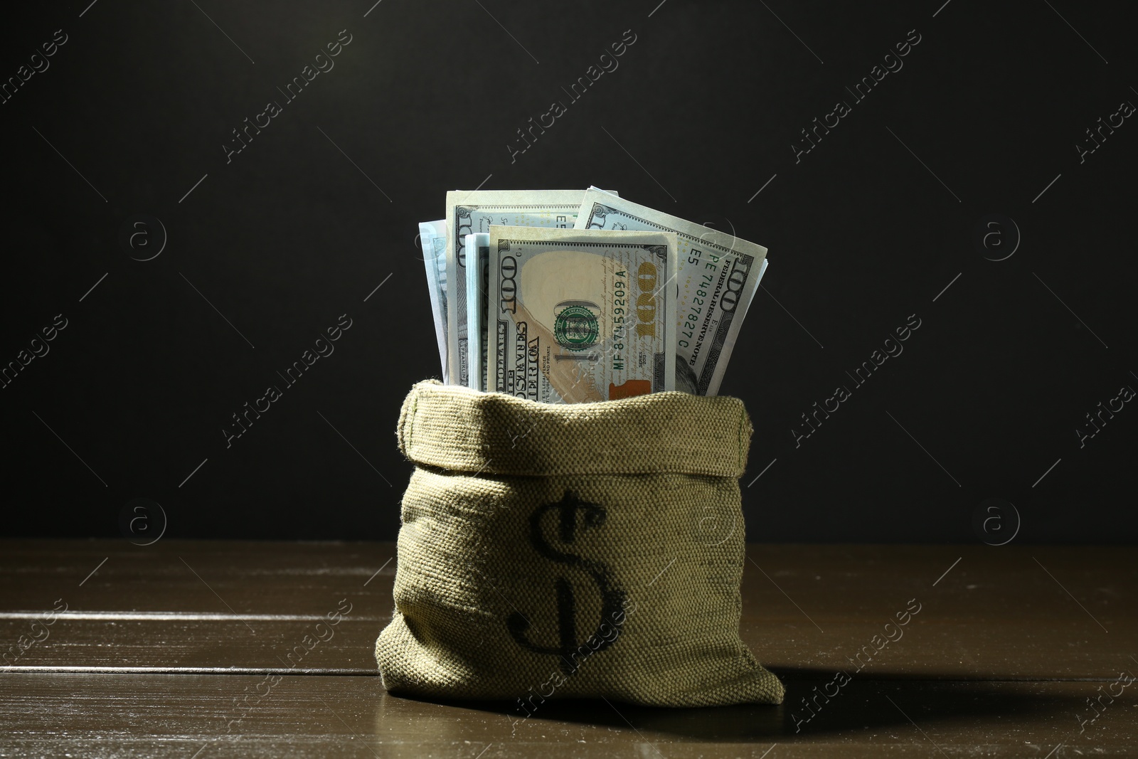 Photo of Dollar banknotes in sack on wooden table against dark background