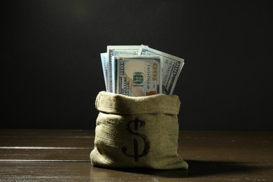 Photo of Dollar banknotes in sack on wooden table against dark background