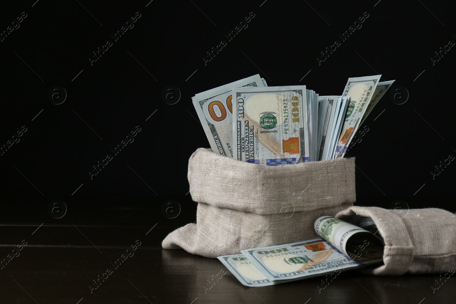 Photo of Dollar banknotes in sacks on wooden table against black background, space for text