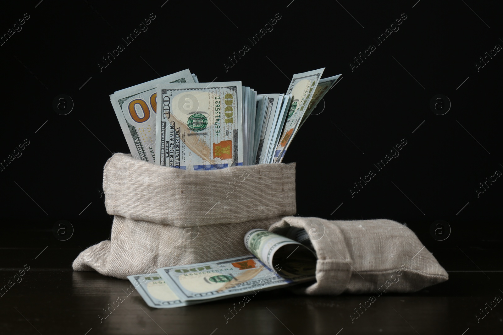 Photo of Dollar banknotes in sacks on wooden table against black background