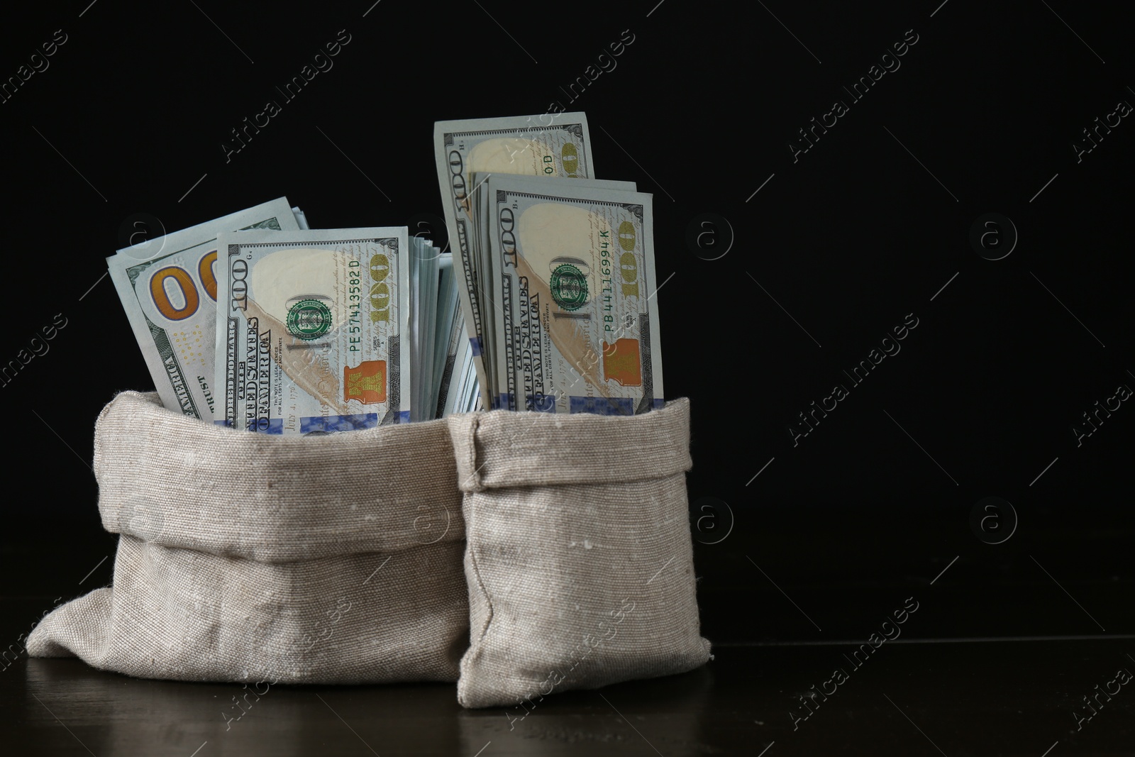 Photo of Dollar banknotes in sacks on wooden table against black background, space for text