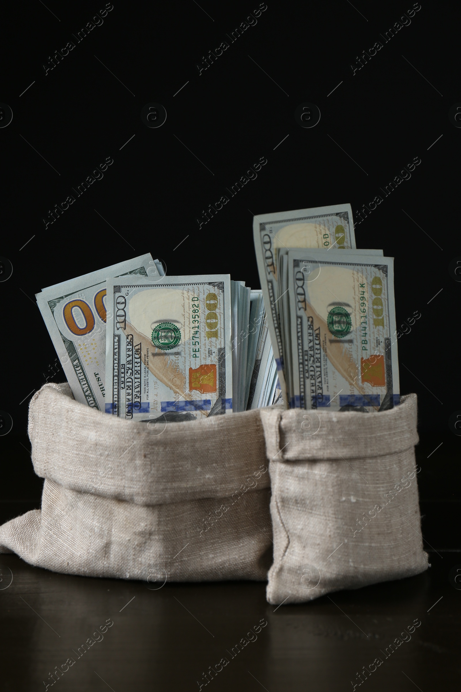 Photo of Dollar banknotes in sacks on wooden table against black background