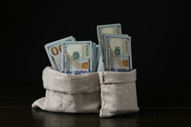 Photo of Dollar banknotes in sacks on wooden table against black background