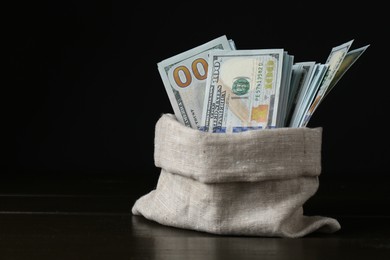 Photo of Dollar banknotes in sack on wooden table against black background