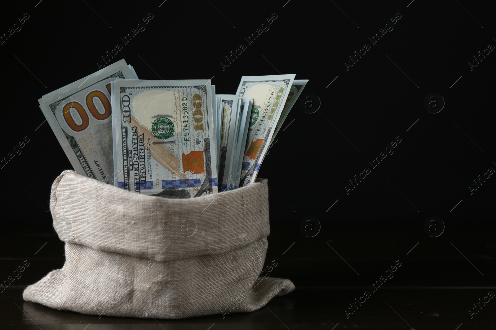 Photo of Dollar banknotes in sack on wooden table against black background, space for text