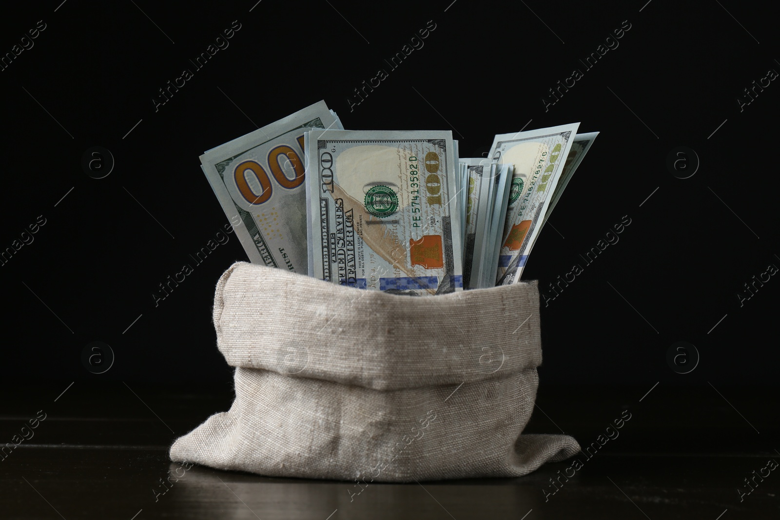 Photo of Dollar banknotes in sack on wooden table against black background