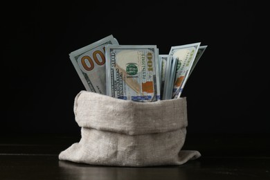 Photo of Dollar banknotes in sack on wooden table against black background