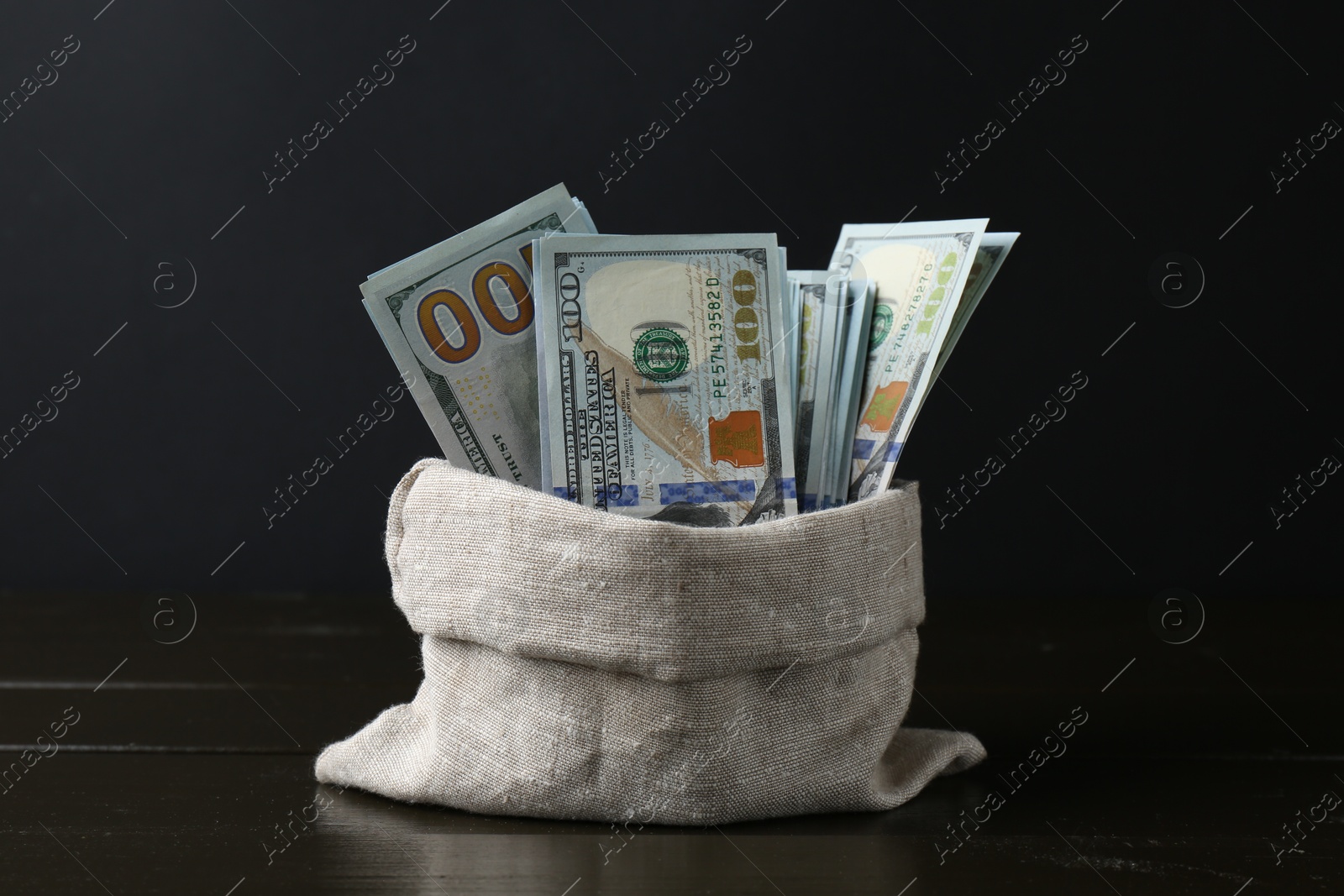 Photo of Dollar banknotes in sack on wooden table against black background