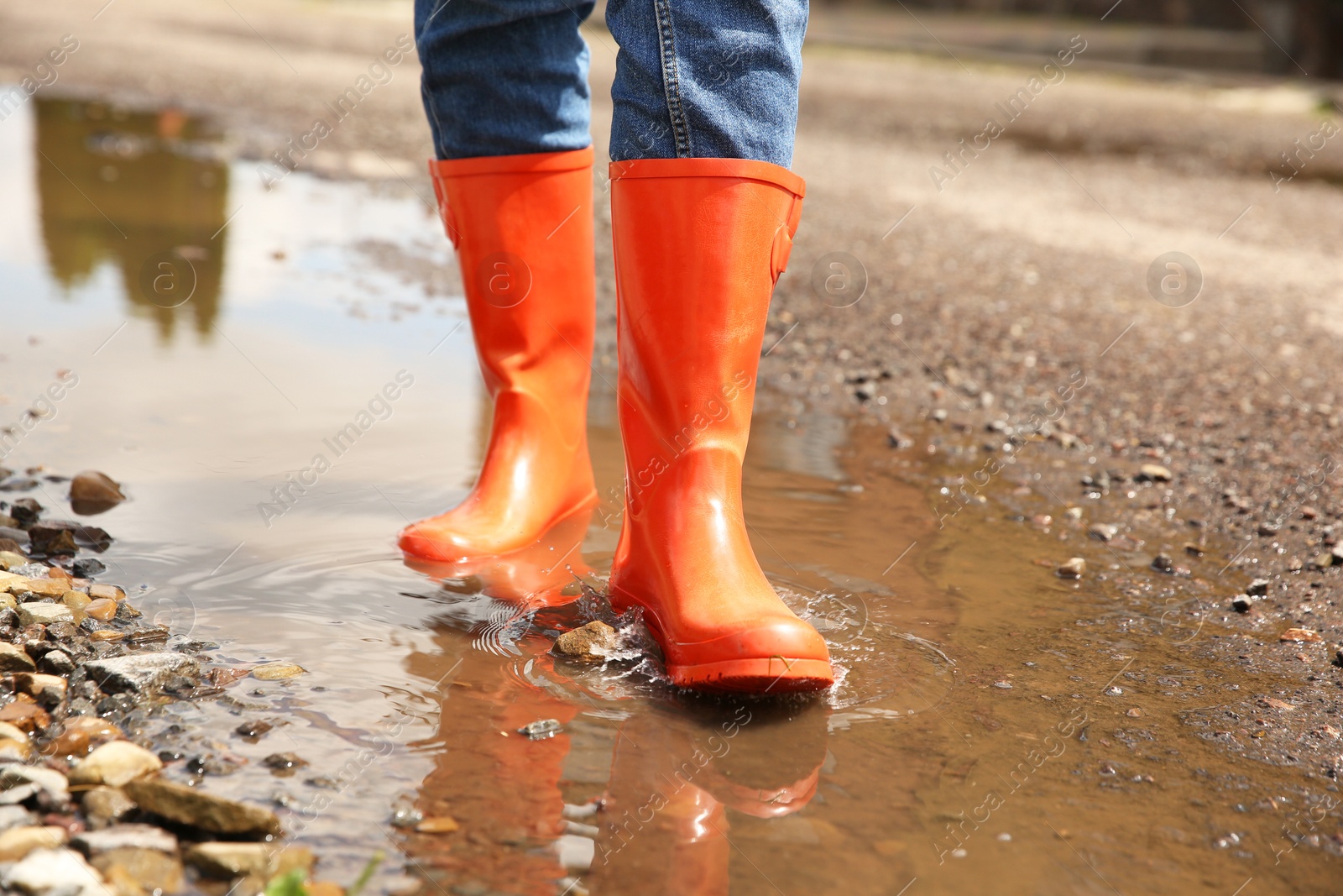 Photo of Woman wearing orange rubber boots standing in puddle outdoors, closeup