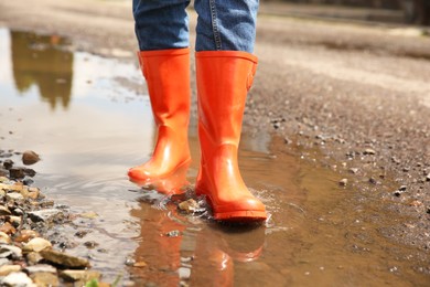 Photo of Woman wearing orange rubber boots standing in puddle outdoors, closeup