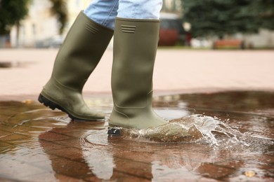 Photo of Woman wearing rubber boots walking in puddle outdoors, closeup