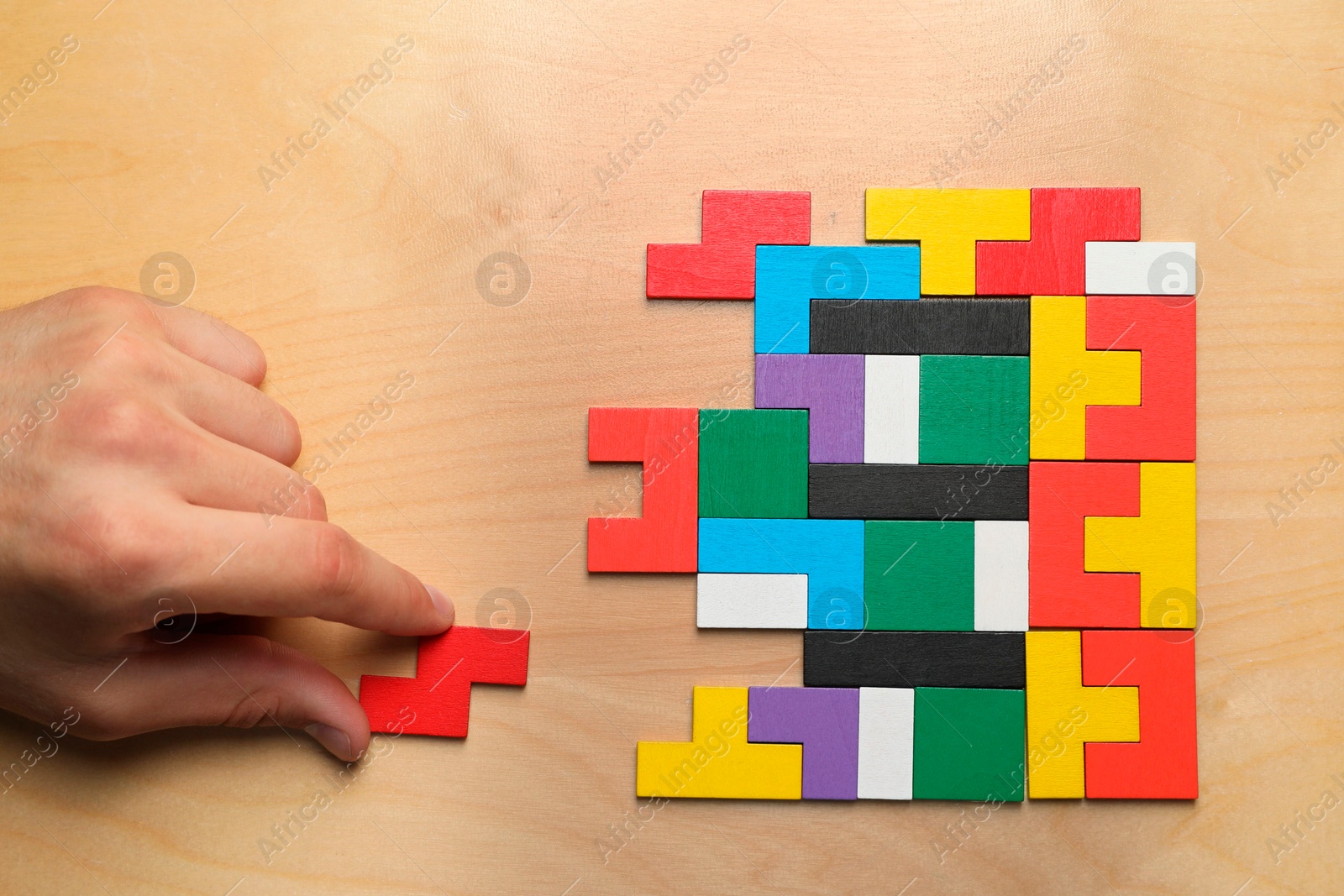 Photo of Woman doing colorful puzzle at wooden table, top view