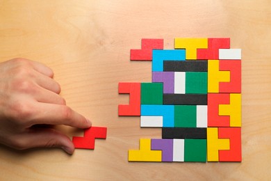 Woman doing colorful puzzle at wooden table, top view