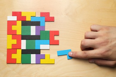 Photo of Woman doing colorful puzzle at wooden table, top view