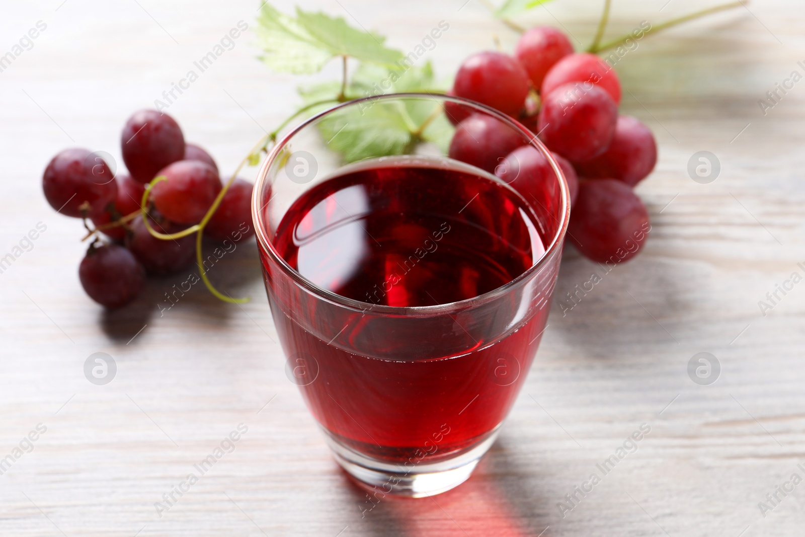 Photo of Tasty grape juice in glass and berries on light wooden table, closeup