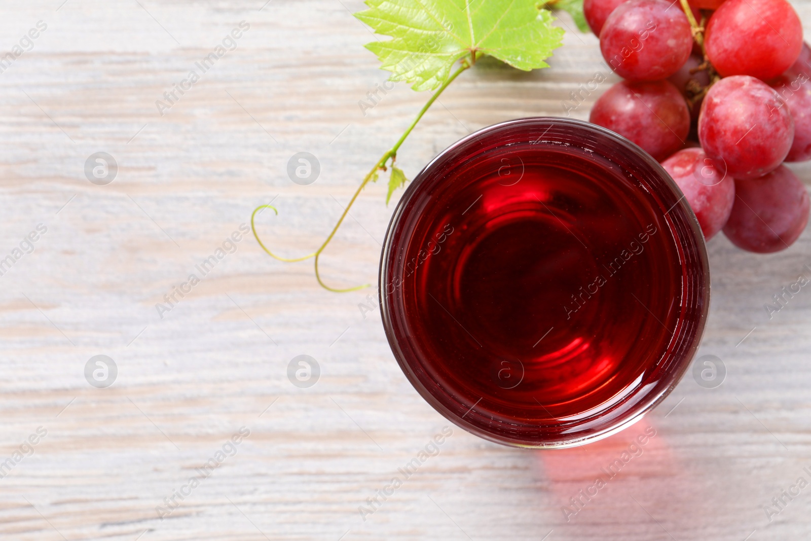 Photo of Tasty grape juice in glass, leaf and berries on light wooden table, flat lay. Space for text