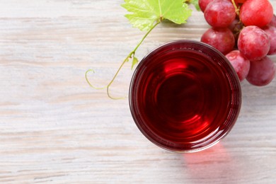 Tasty grape juice in glass, leaf and berries on light wooden table, flat lay. Space for text