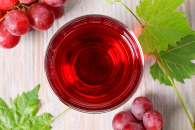 Photo of Tasty grape juice in glass, leaves and berries on light wooden table, flat lay