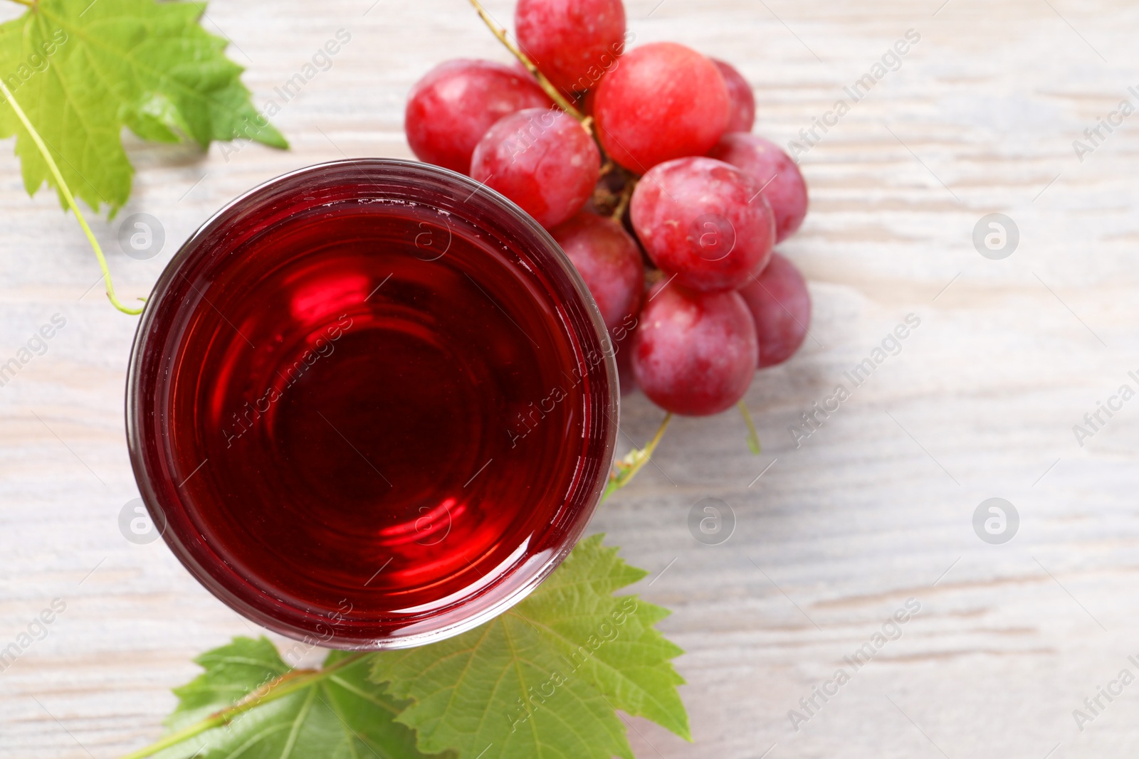 Photo of Tasty grape juice in glass, leaves and berries on light wooden table, flat lay. Space for text