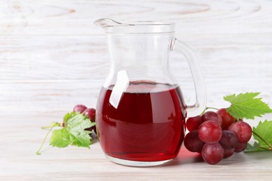 Photo of Tasty grape juice in jar, leaves and berries on light wooden table, closeup