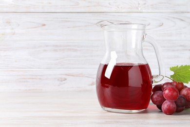 Photo of Tasty grape juice in jar, leaf and berries on light wooden table. Space for text