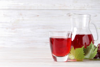 Tasty grape juice, leaves and berries on light wooden table. Space for text