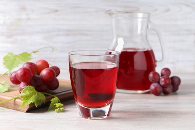 Photo of Tasty grape juice, leaves and berries on light wooden table