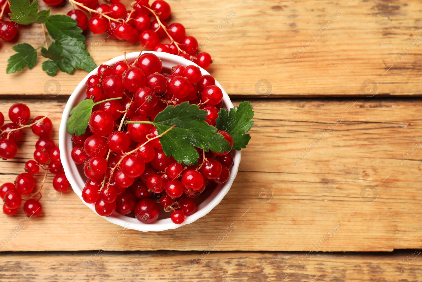 Photo of Fresh red currants and green leaves on wooden table, top view. Space for text