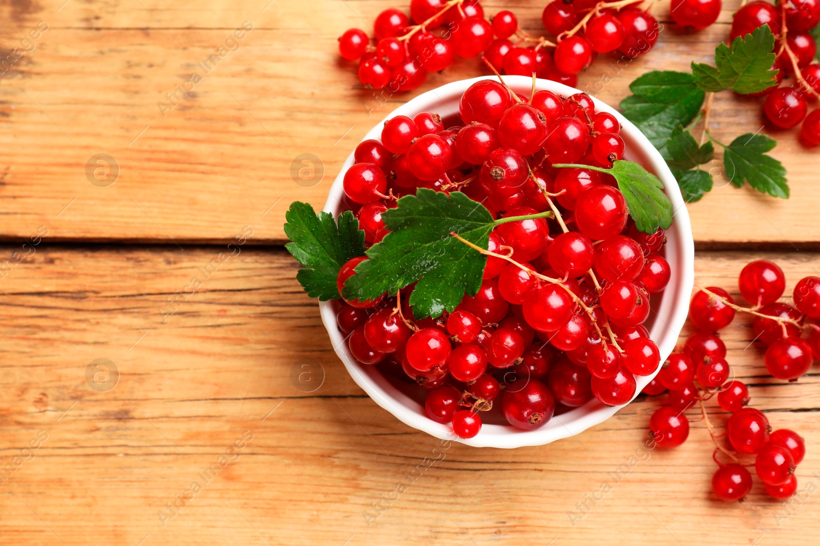 Photo of Fresh red currants and green leaves on wooden table, top view. Space for text