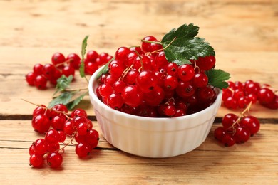 Photo of Fresh red currants and green leaves on wooden table, closeup