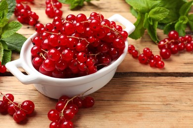 Photo of Fresh red currants in bowl and mint on wooden table, closeup