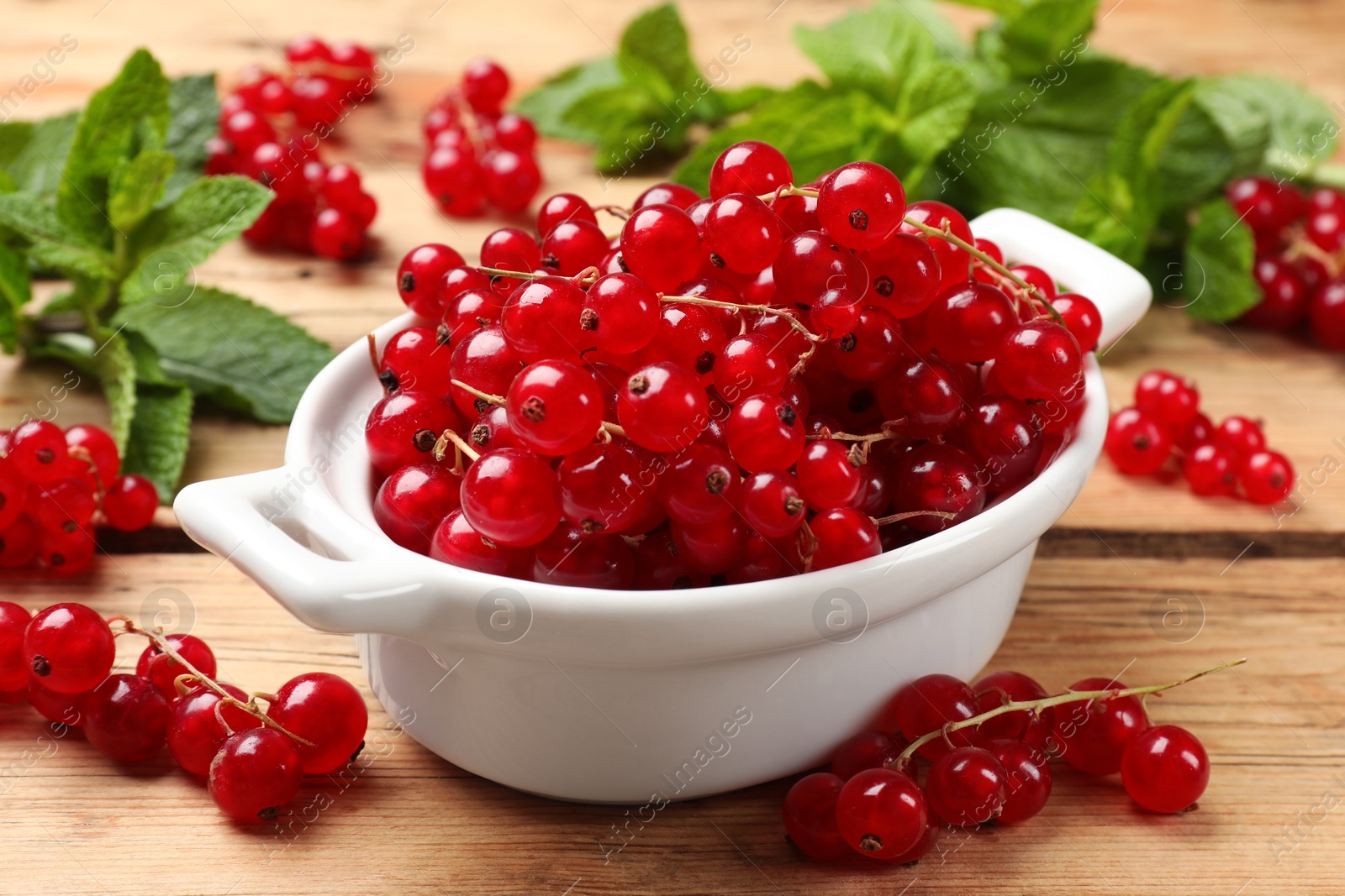 Photo of Fresh red currants in bowl and mint on wooden table, closeup