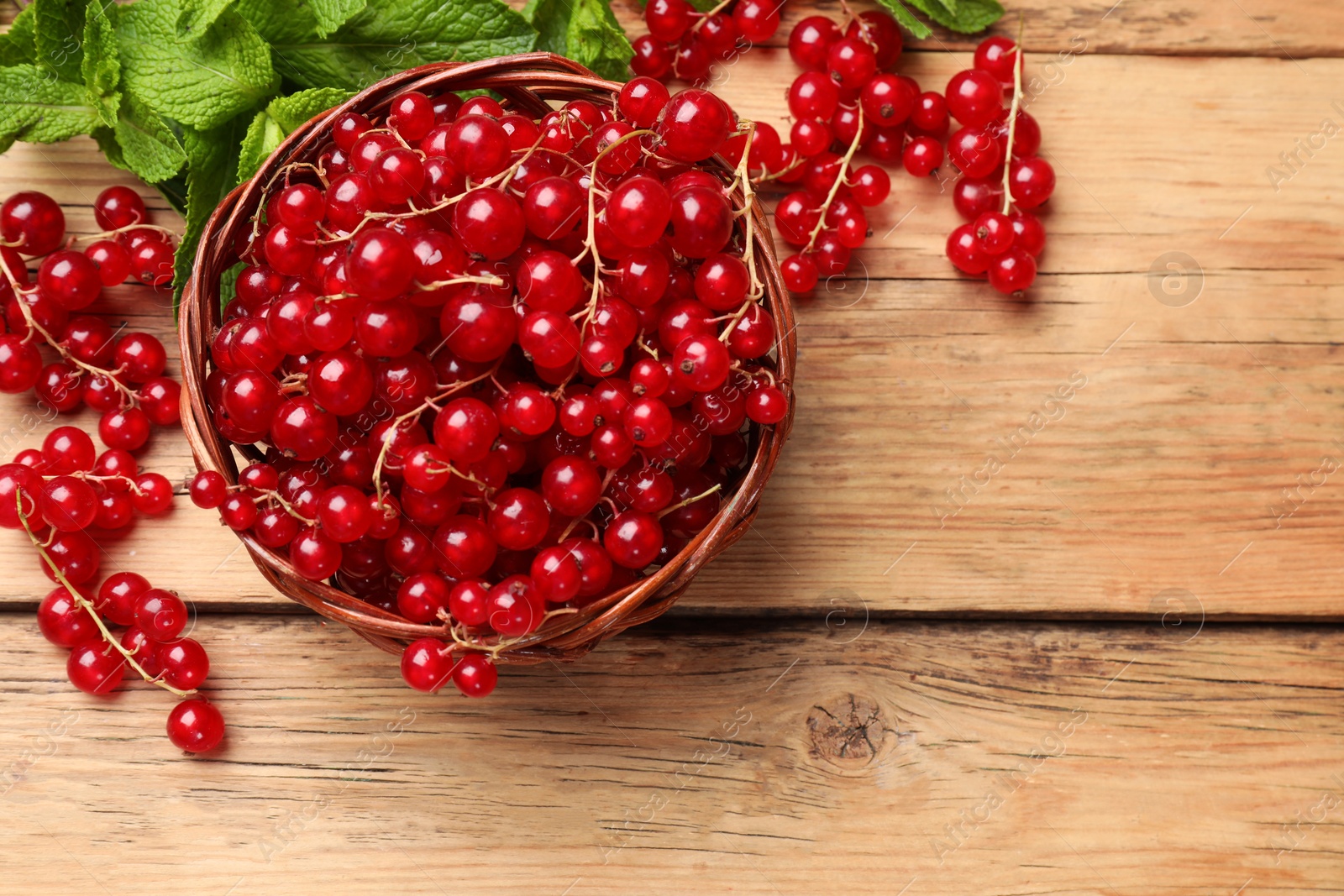 Photo of Fresh red currants in basket and mint on wooden table, flat lay. Space for text