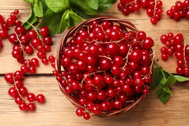 Photo of Fresh red currants in basket and mint on wooden table, flat lay