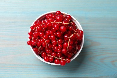 Photo of Fresh red currants in bowl on light blue wooden table, top view