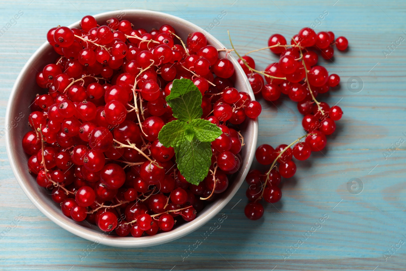 Photo of Fresh red currants in bowl and mint on light blue wooden table, top view