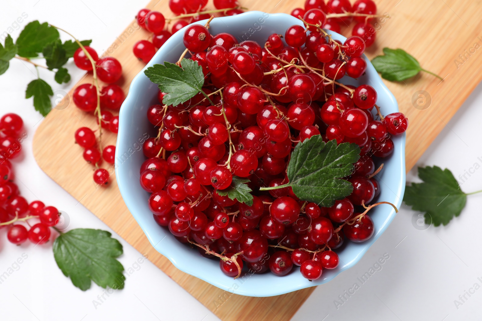 Photo of Fresh red currants in bowl and green leaves on white table, top view