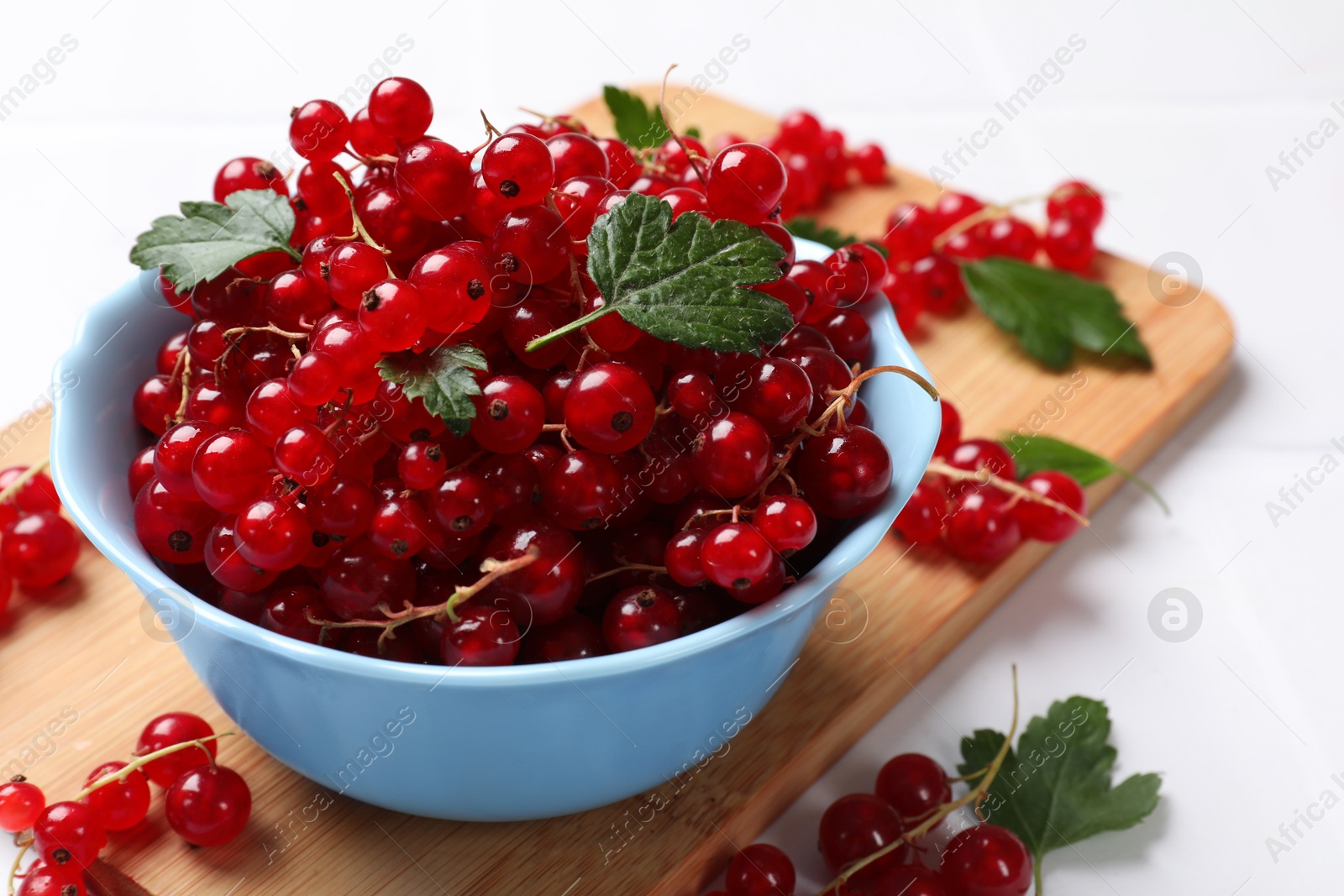 Photo of Fresh red currants in bowl and green leaves on white table, closeup