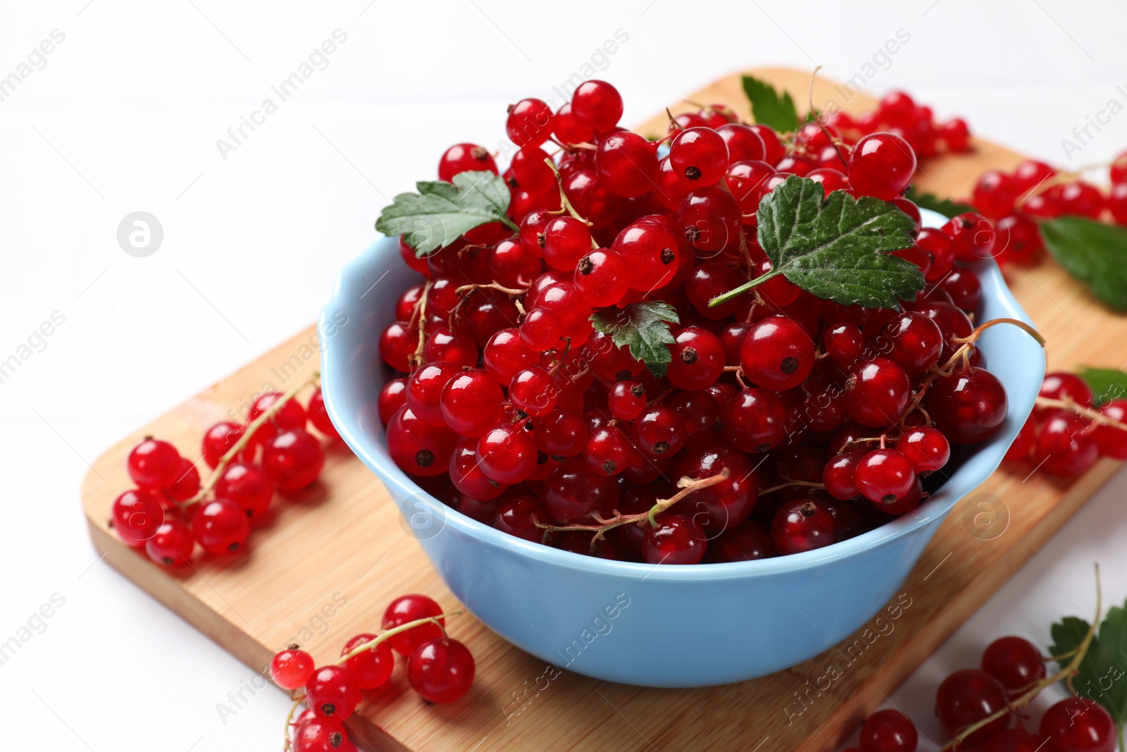 Photo of Fresh red currants in bowl and green leaves on white table, closeup