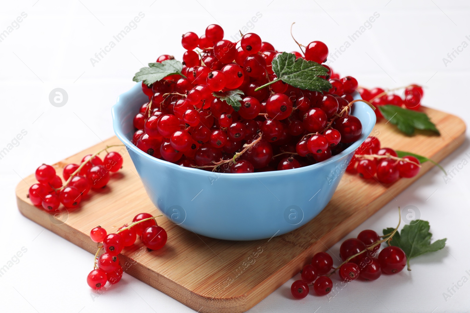 Photo of Fresh red currants in bowl and green leaves on white table, closeup