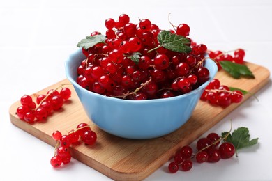 Photo of Fresh red currants in bowl and green leaves on white table, closeup