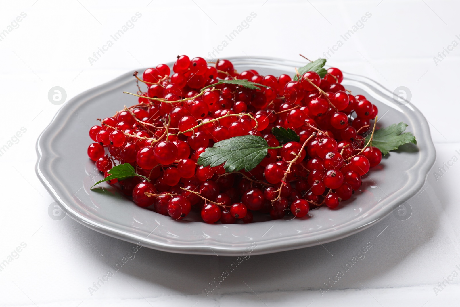 Photo of Fresh red currants and leaves on white table, closeup