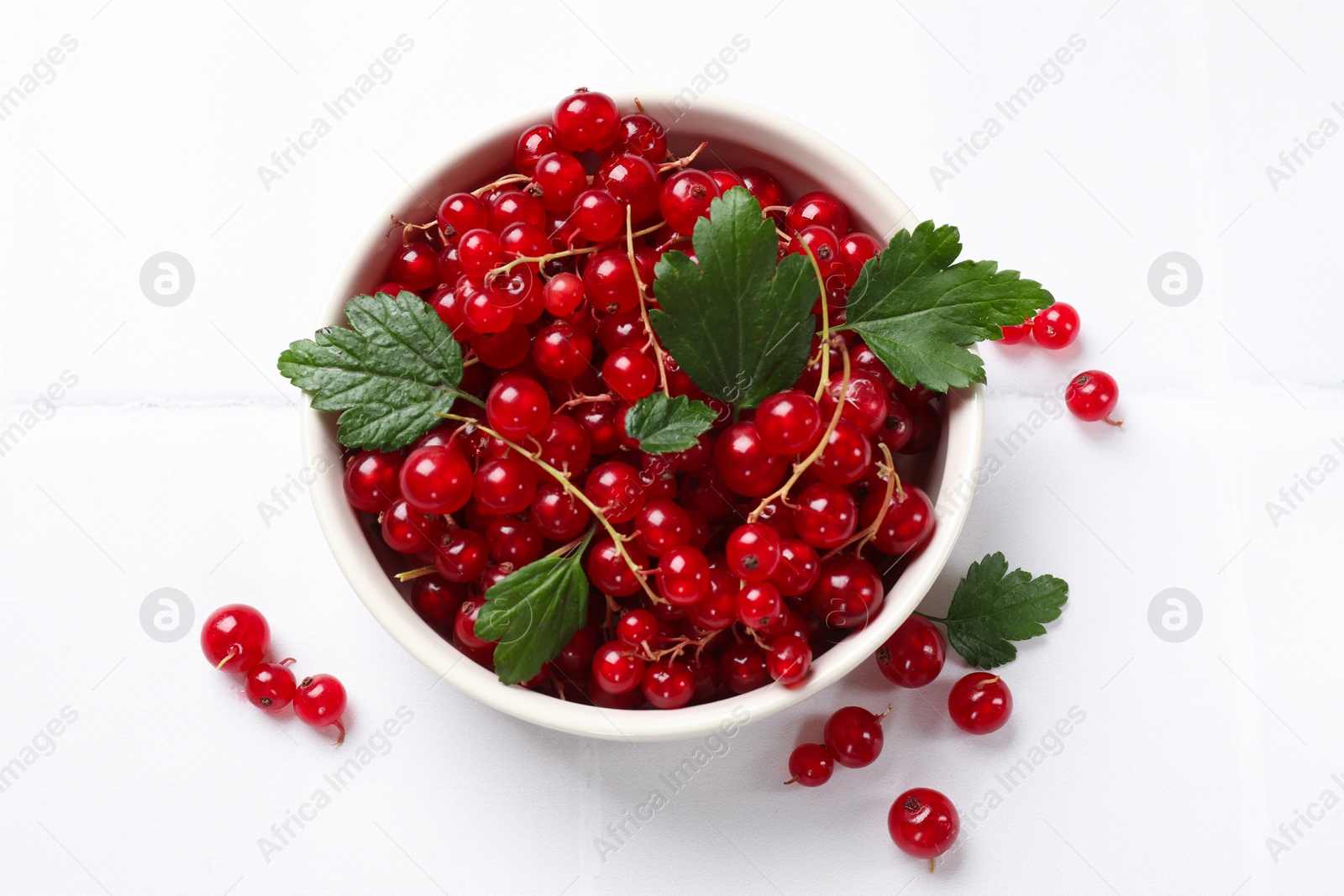 Photo of Fresh red currants and leaves in bowl on white table, top view