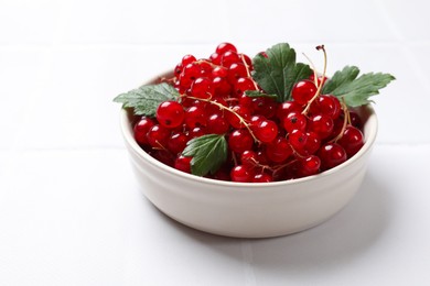 Photo of Fresh red currants and leaves in bowl on white table, closeup