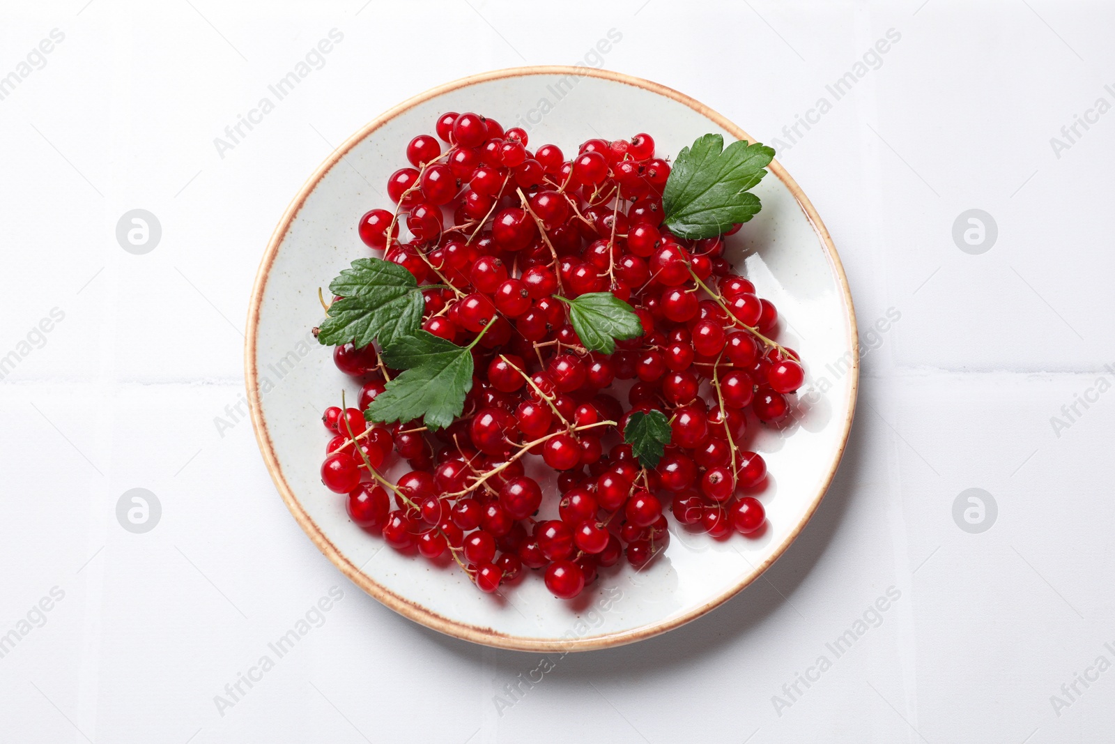 Photo of Fresh red currants and green leaves on white table, top view