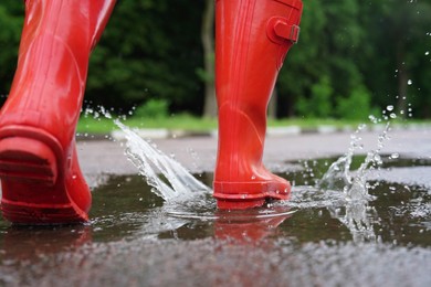 Photo of Woman wearing red rubber boots walking in puddle outdoors, closeup