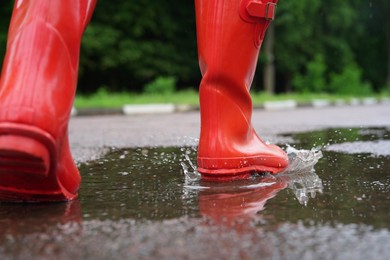 Photo of Woman wearing red rubber boots walking in puddle outdoors, closeup