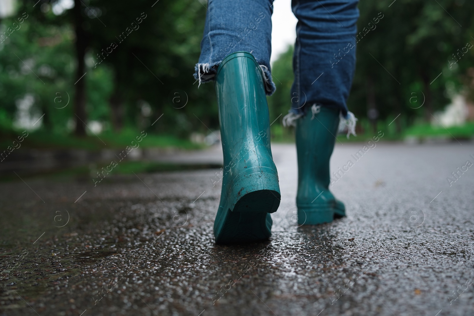 Photo of Woman in turquoise rubber boots walking on wet road, closeup. Space for text