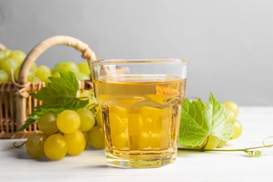 Ripe grapes and glass of tasty juice on white wooden table