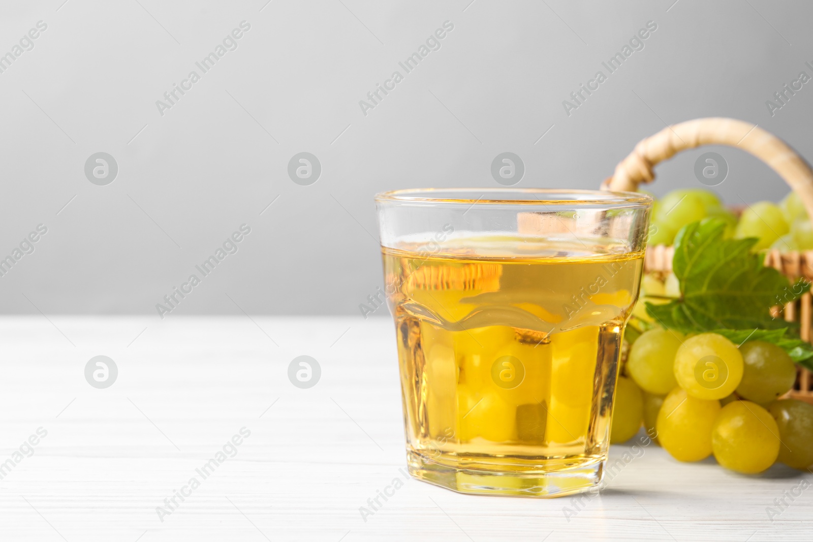 Photo of Ripe grapes and glass of tasty juice on white wooden table. Space for text